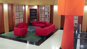 A lobby with red sofas, a glass coffee table, a large orange pillar, and framed artwork on the walls.