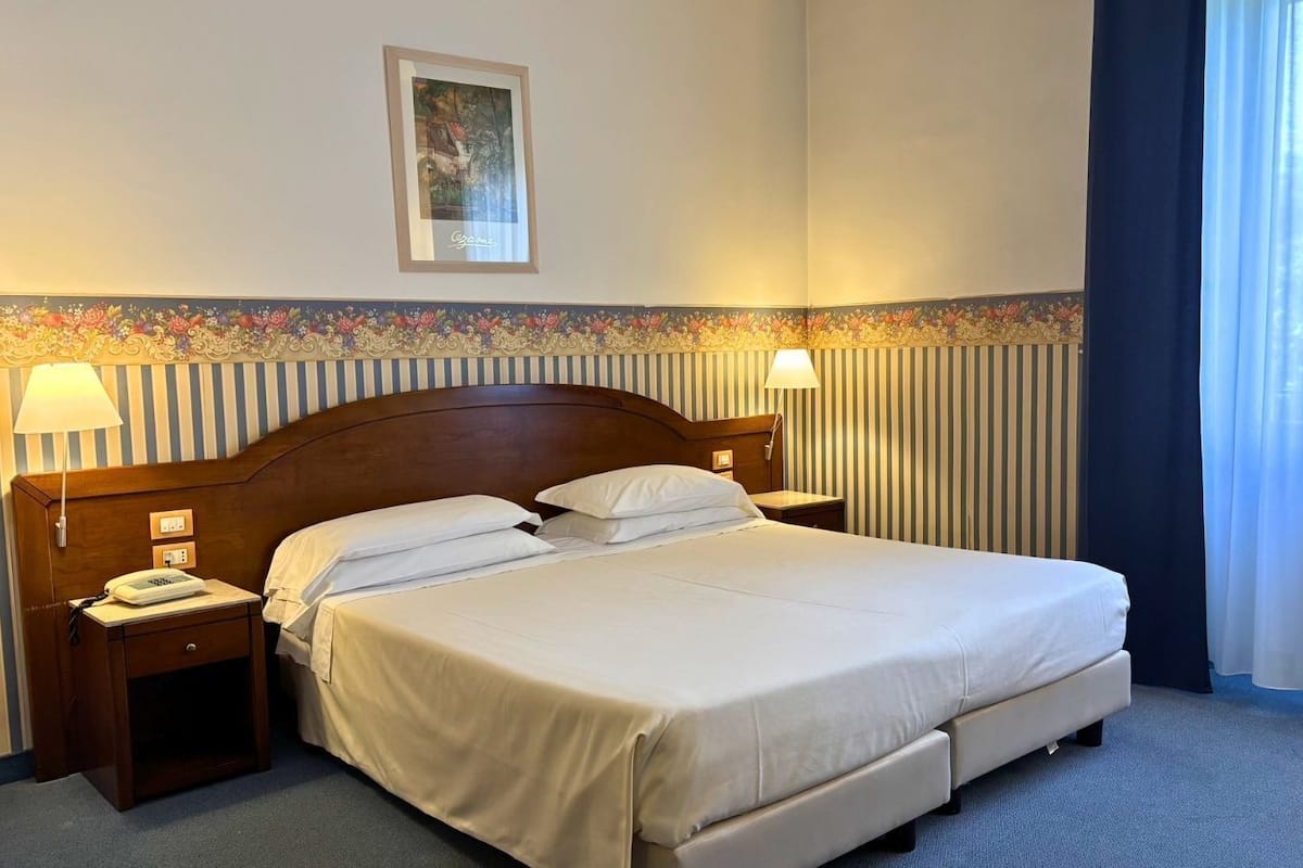 A hotel room with a large bed, two bedside tables with lamps, a framed picture on the wall, and a striped border along the lower wall.