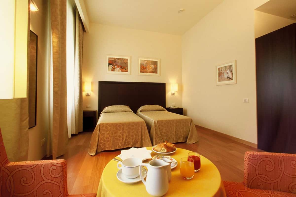A hotel room with two single beds, a dining table with breakfast items, and a view of the hallway.