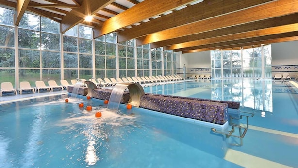 An indoor swimming pool with a water slide, lounge chairs, and a view of trees through large windows. - Hotel Terme (Montechiarugolo)