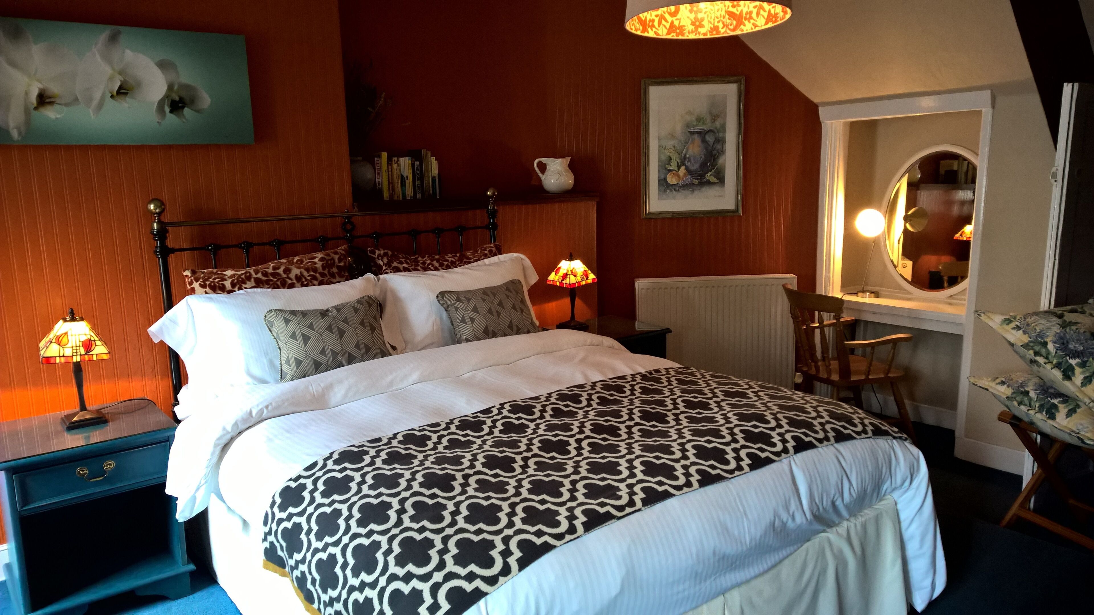 Een slaapkamer met een bed, bedlampen, een stoel, een tafel en een schilderij aan de muur.