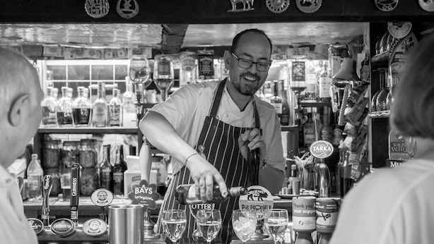 A bartender pouring drinks at a bar with various bottles and glasses. - Lifton Hall (Lifton)