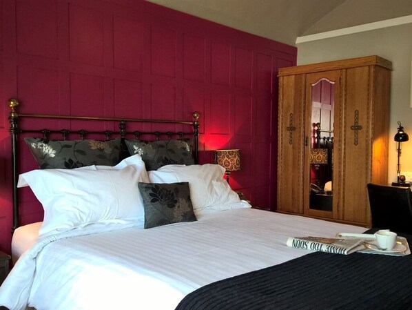 A hotel room with a large bed, a wooden wardrobe, and a mirror.