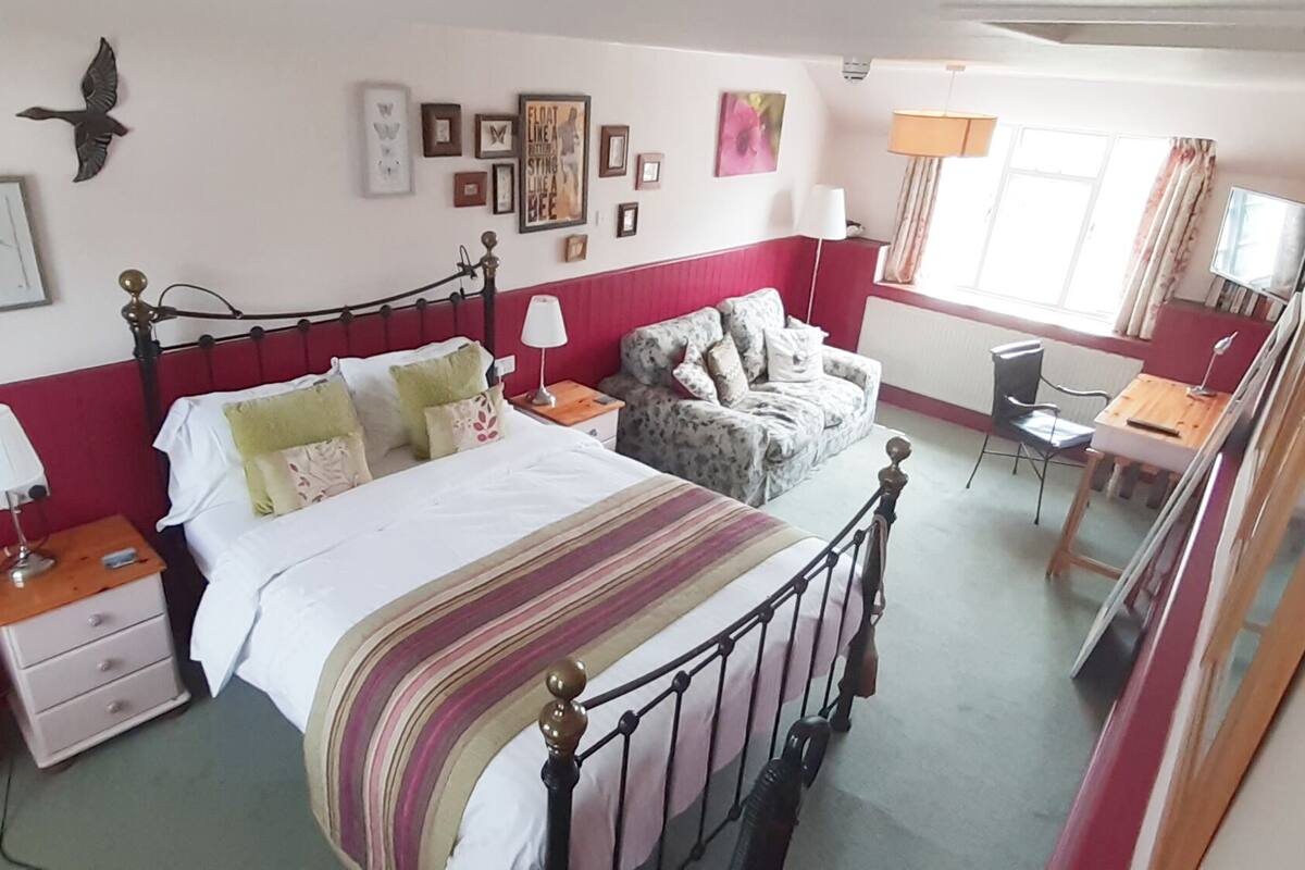 A bedroom with a bed, bedside tables, a chair, a desk, and a window.