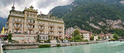 Un hotel grande de varios pisos con balcones y un río al frente.