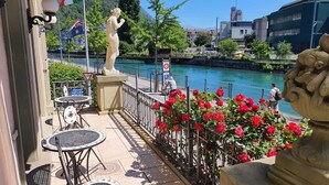 Terraza a la orilla del río con mesas al aire libre, una estatua y vistas del río.
