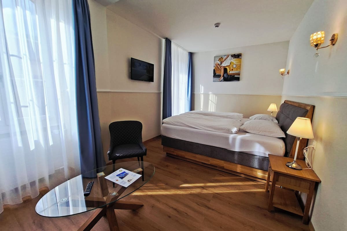 A hotel room with a bed, a chair, a glass table with a menu, and a TV on the wall.