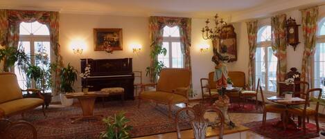 A spacious living room with a piano, comfortable seating, and decorative elements like plants and artwork.