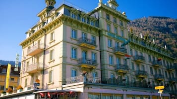 Un hotel de varios pisos con balcones y montañas al fondo.