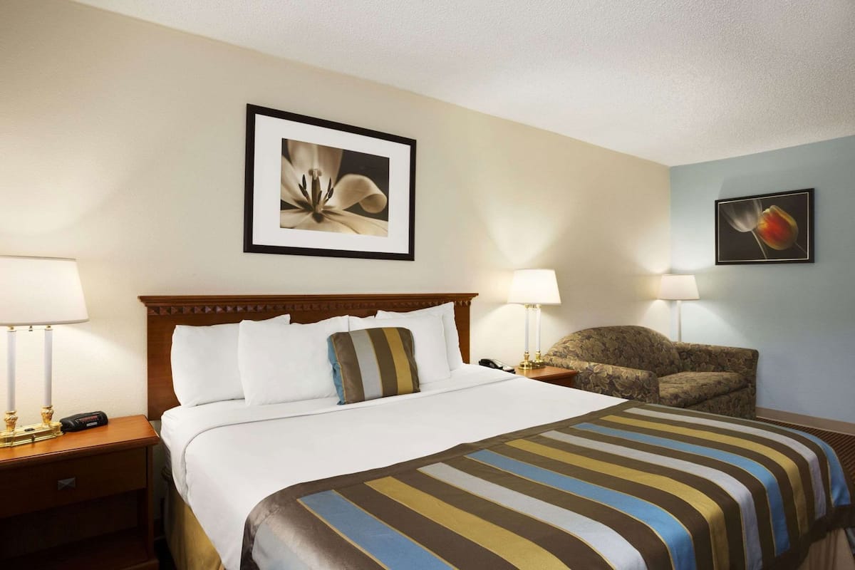 Una habitación de hotel con una cama, dos mesitas de noche, una silla y dos lámparas de pared.