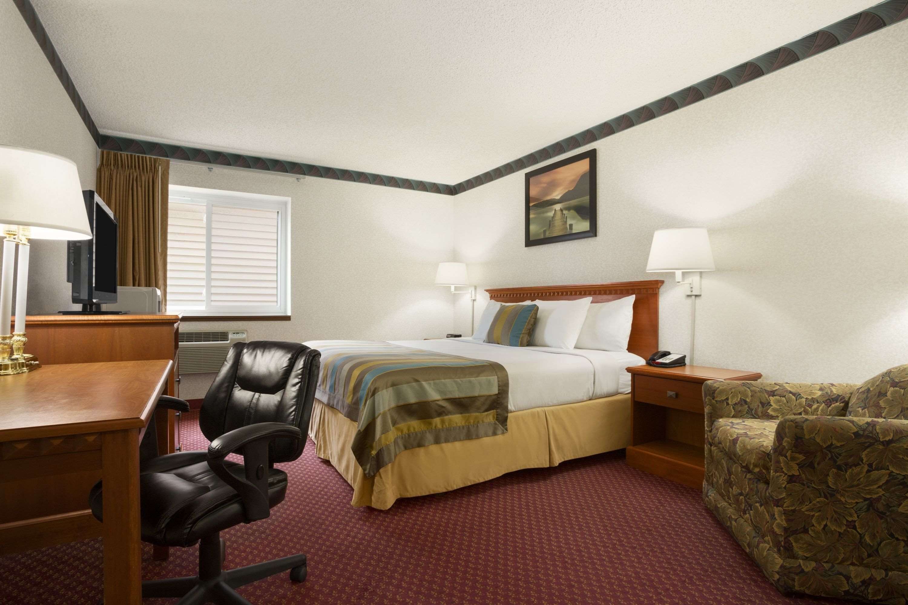 A hotel room with a bed, a desk, a chair, a television, and a window with blinds.