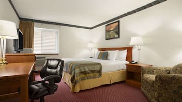 A hotel room with a bed, a desk, a chair, a television, and a window with blinds.