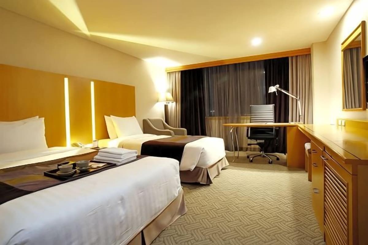 A hotel room with two beds, a desk, a chair, a lamp, and a mirror.