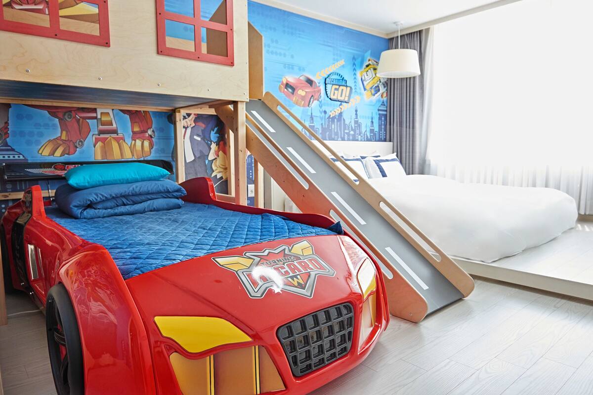 A child's bedroom with a bed designed like a race car, a cityscape mural, and a window with curtains.