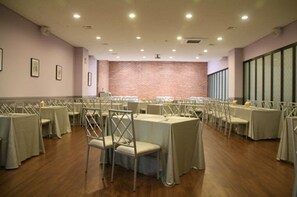 A conference room with multiple tables and chairs, a brick accent wall, and large windows.