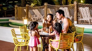 A family dining at an outdoor table with yellow chairs, surrounded by a pool and a fence. - Hotel Miranda (Icheon)