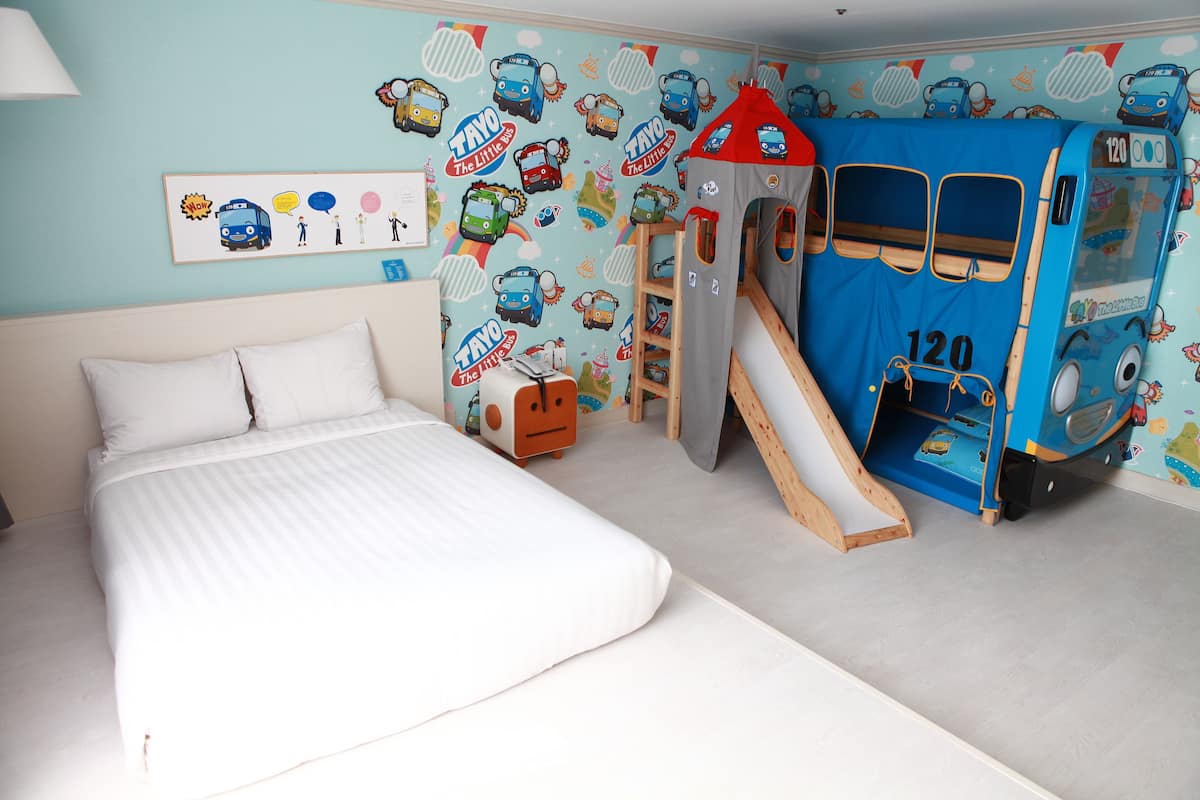 A child's bedroom with a bed, a playhouse, and a wall decorated with cartoon vehicles.
