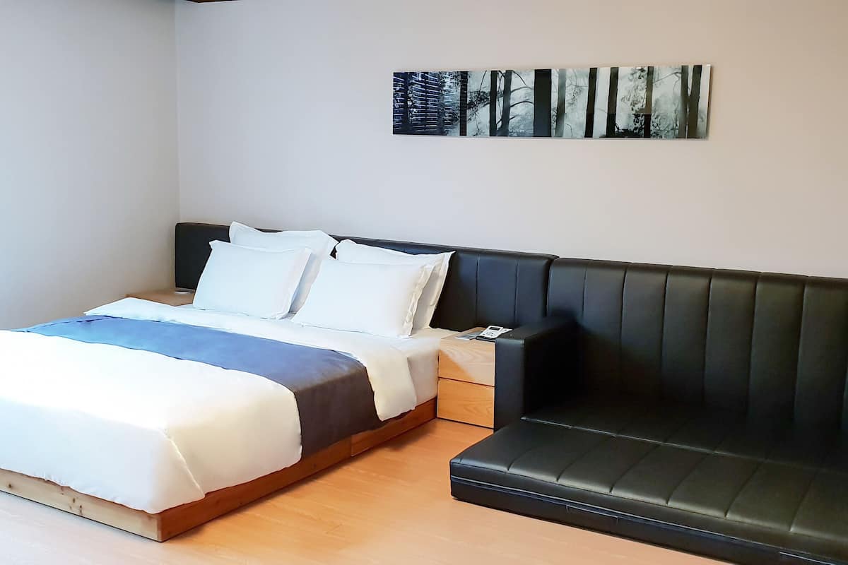 A bedroom with a bed, a black leather sofa, and a wall-mounted artwork.