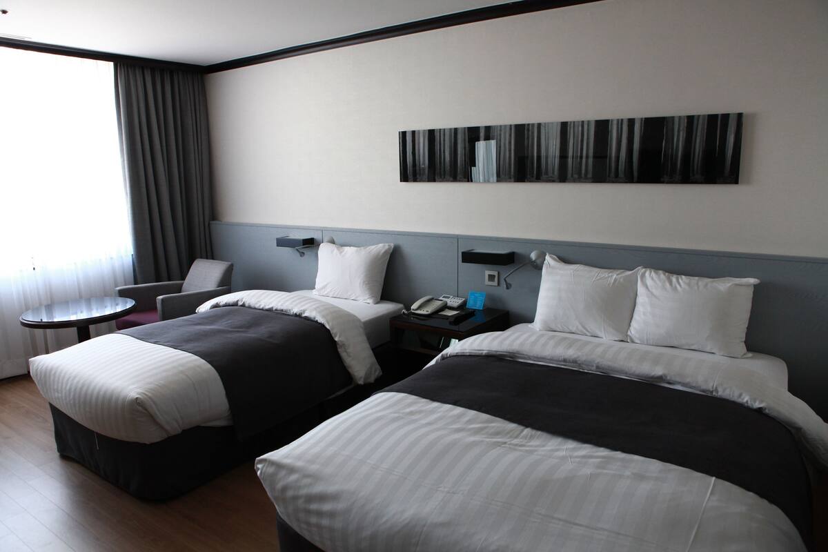 A hotel room with two beds, a desk, a chair, a small table, and a large window with curtains.