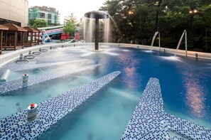 A swimming pool with multiple jets, a water fountain, and a tiled deck.