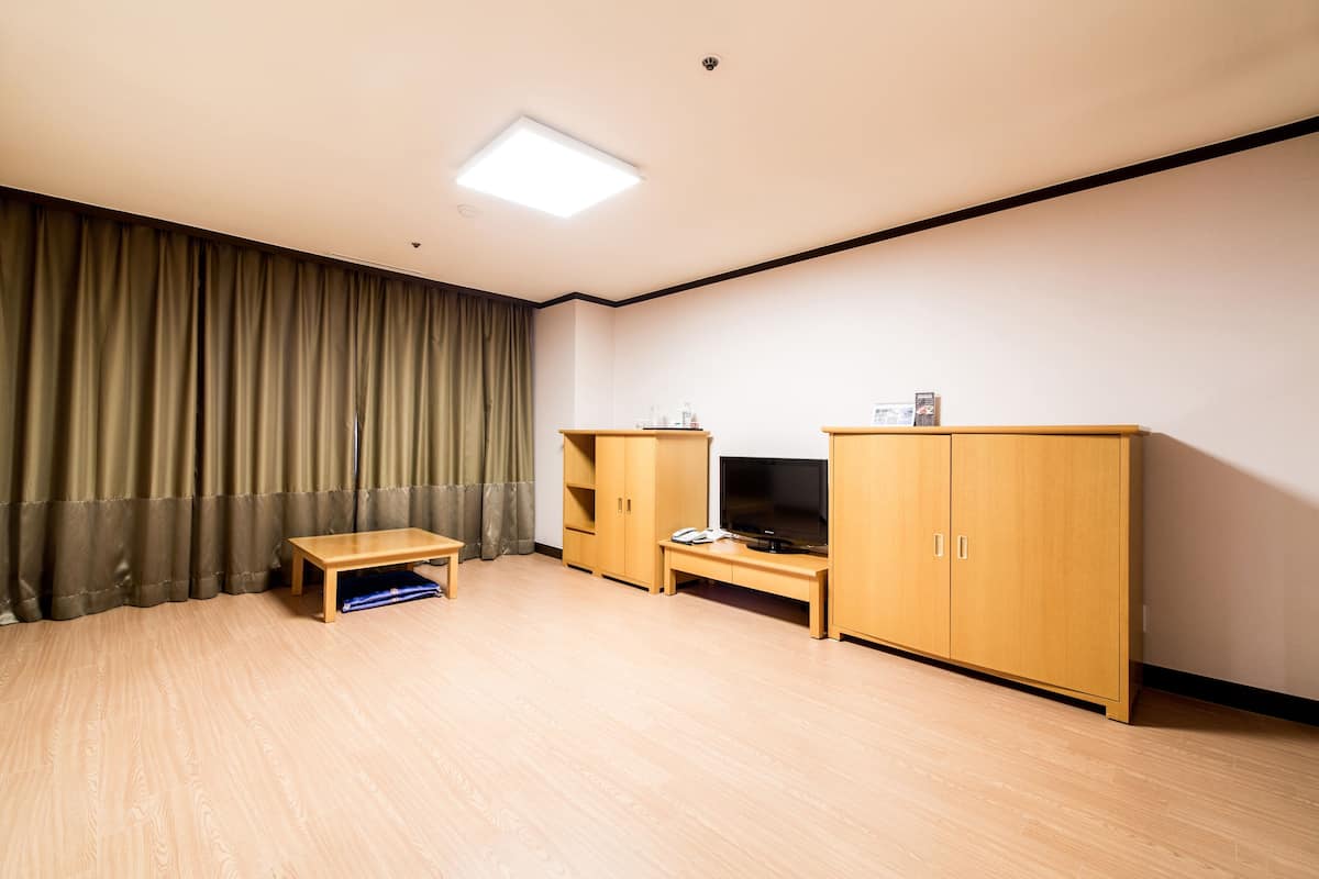 A room with a wooden floor, a small wooden table, a TV stand, and a large wardrobe.