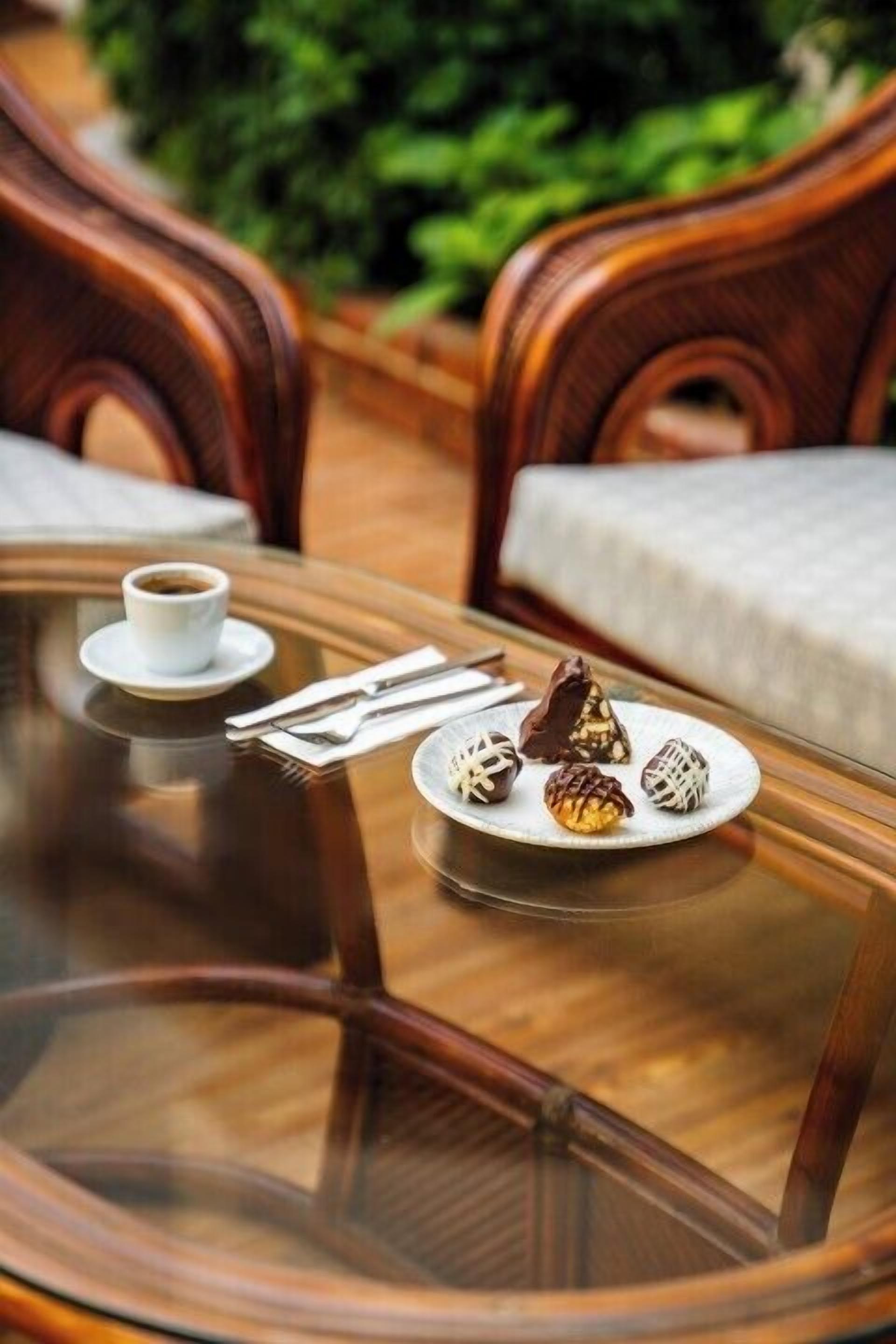 A glass table with a plate of assorted pastries and a cup of coffee.