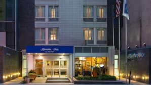 A hotel entrance with a sign reading "Hampton Inn by Hilton" and multiple flags, including the American flag. - Hampton Inn Madison Square Garden Area Hotel (New York)