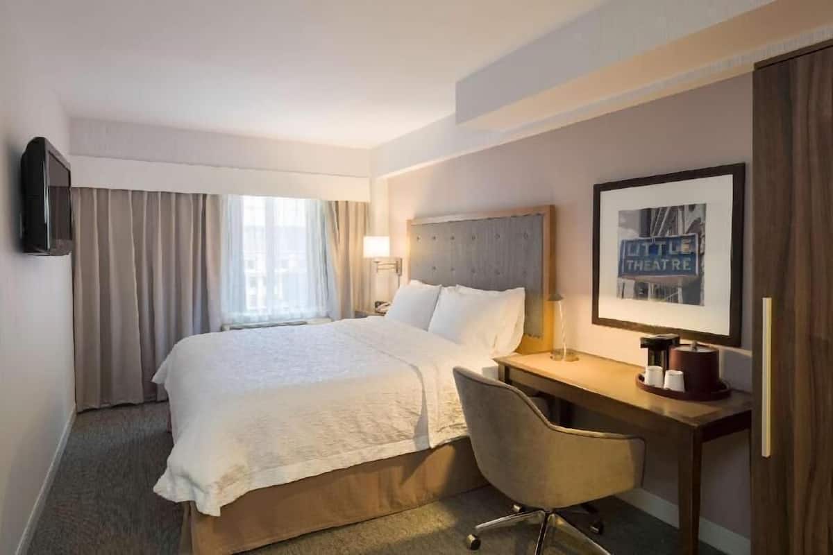 Una habitación de hotel con cama, escritorio, silla, televisor y un cuadro en la pared.