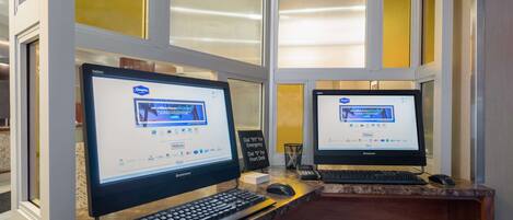 Two computer monitors at a reception desk with a sign indicating a 911 emergency phone.
