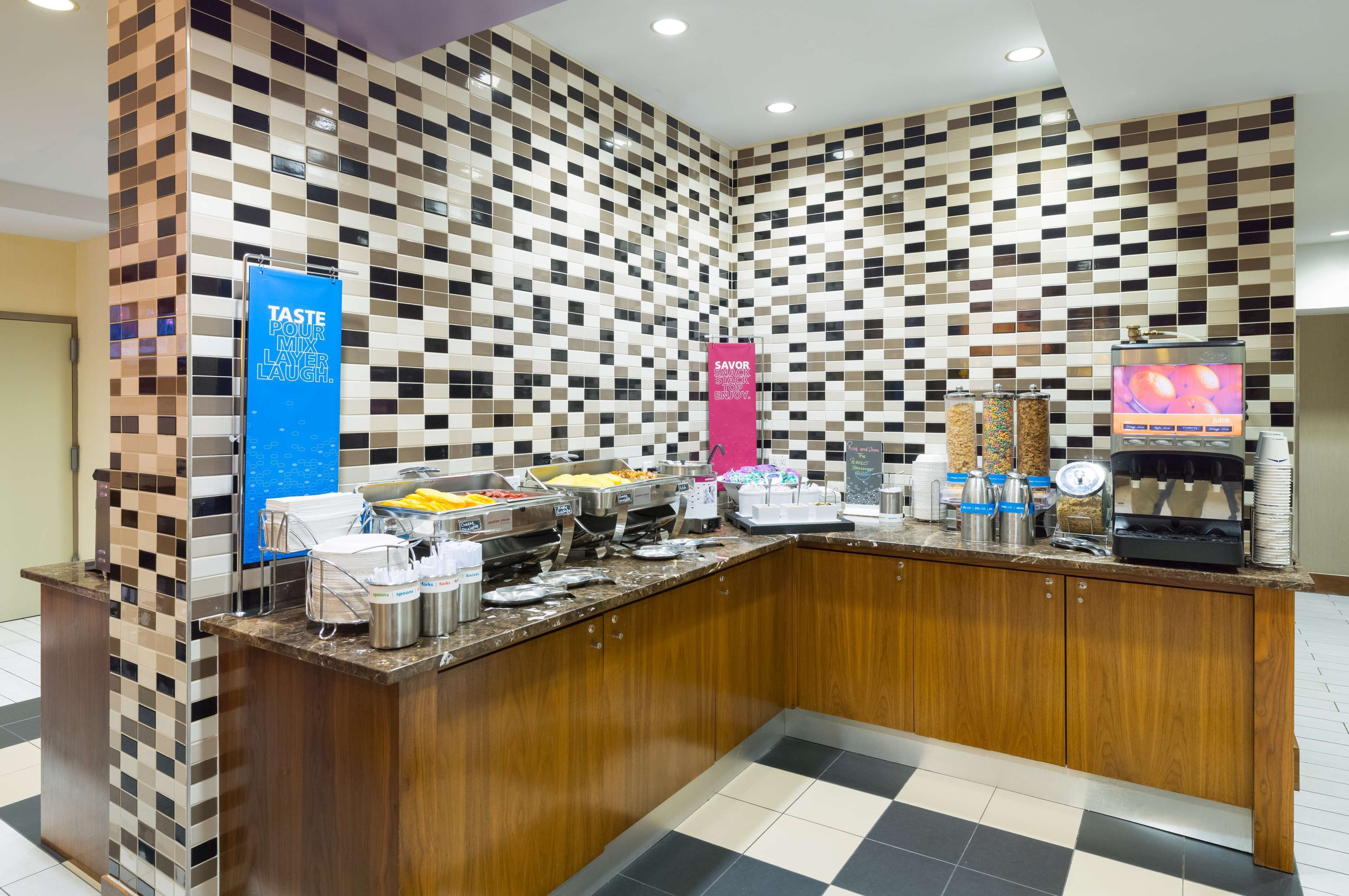 Zona de buffet con pared de baldosas de cuadros, una máquina de café y varios recipientes de comida.