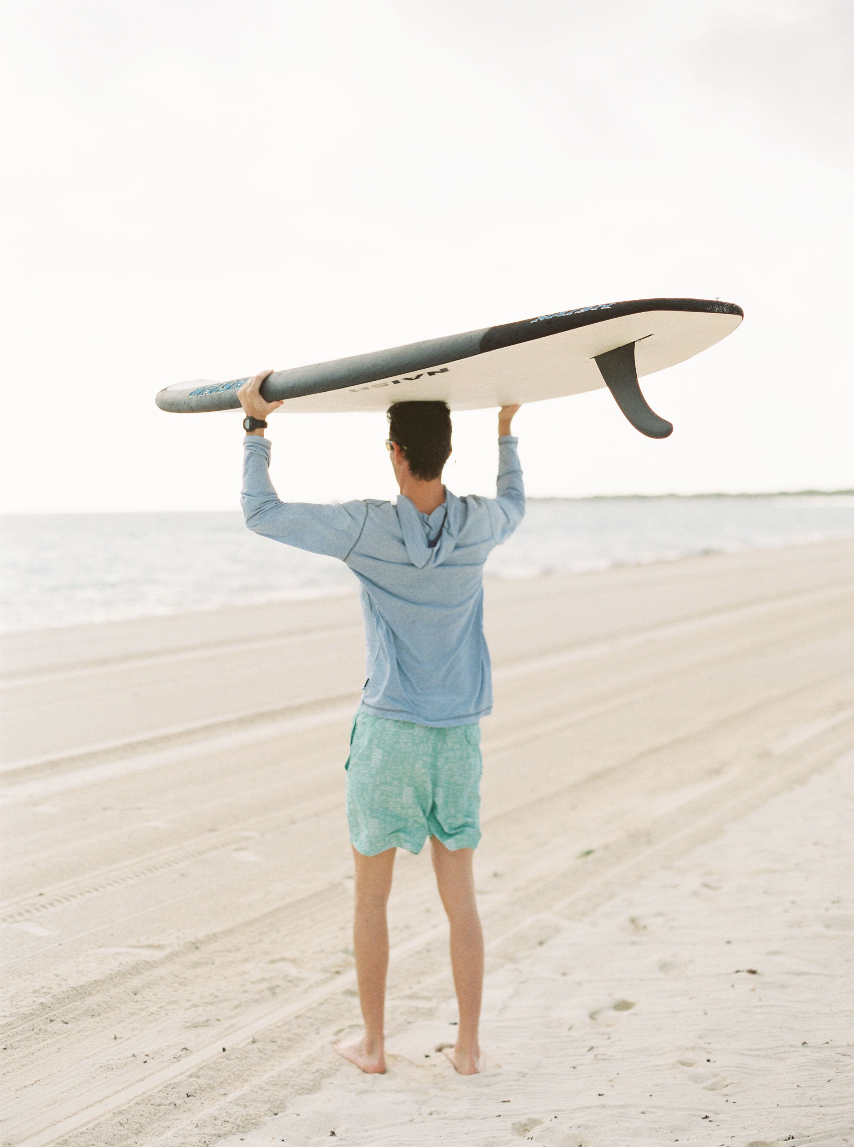 Una persona tiene un’asse da surf sopra la testa su una spiaggia.