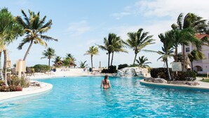 Une piscine entourée de palmiers, avec des chaises longues et une personne dans l’eau.