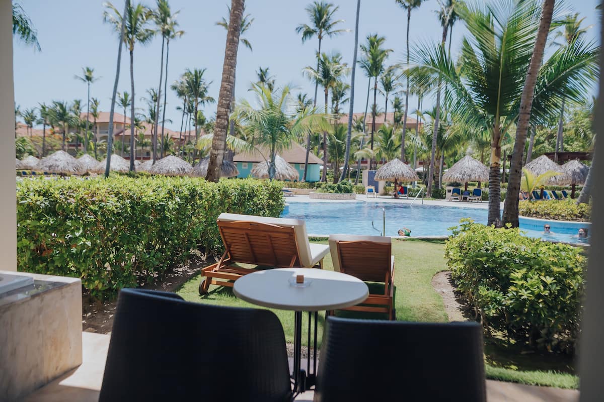 A poolside area with lounge chairs and a table, surrounded by palm trees and a view of a swimming pool.