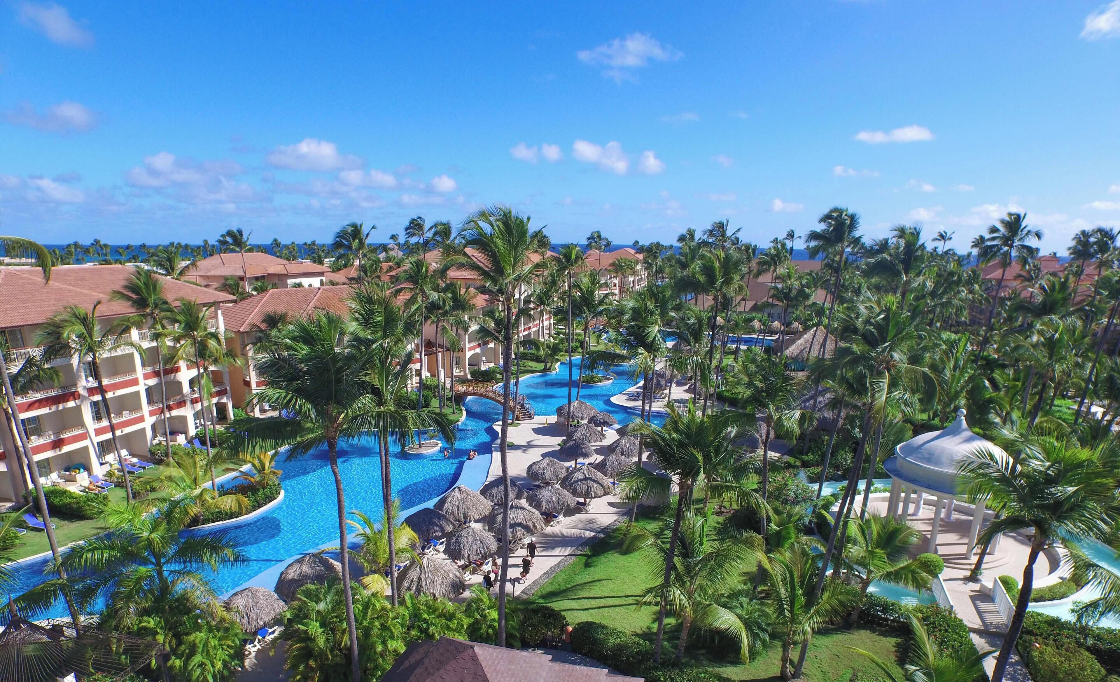 Un resort con varias piscinas, palmeras y vista al océano.