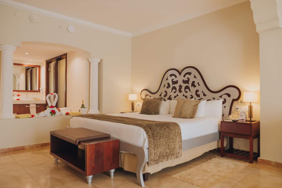 A hotel room with a large bed, bedside tables, a mirror, and a view of the bathroom.
