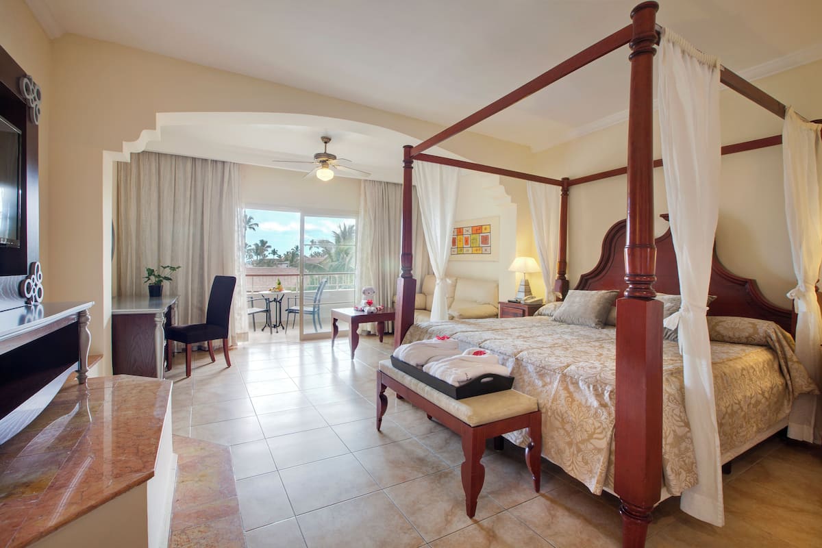 A four-poster bed with a canopy, a television, a desk with a chair, and a dining area with a table and chairs.