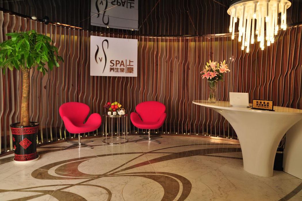 A reception area with a modern design, featuring a reception desk, two red chairs, a potted plant, and a decorative wall with vertical lines.