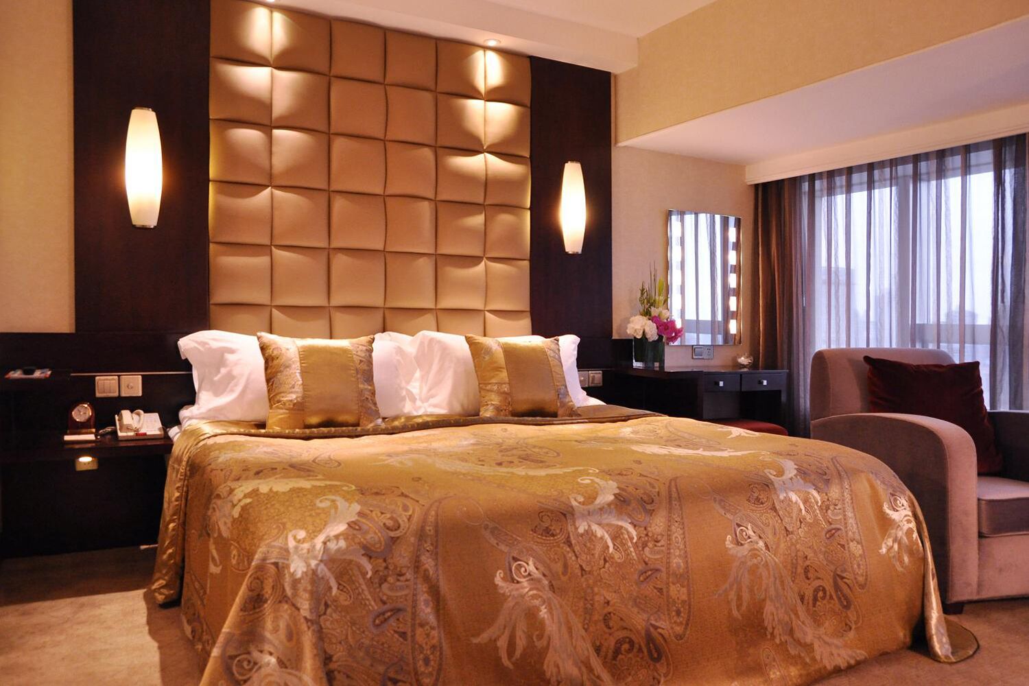 A hotel room with a large bed, a nightstand, a desk, a chair, and a large window with curtains.