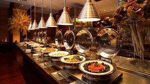 A buffet area with multiple food stations, overhead lighting, and a decorative plant arrangement. - Jinling Purple Mountain Hotel Shanghai (Shanghai)