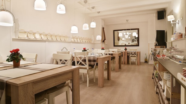 A restaurant with multiple tables and chairs, pendant lights, and a counter with dishes. - Hotel Corel (The Hague)