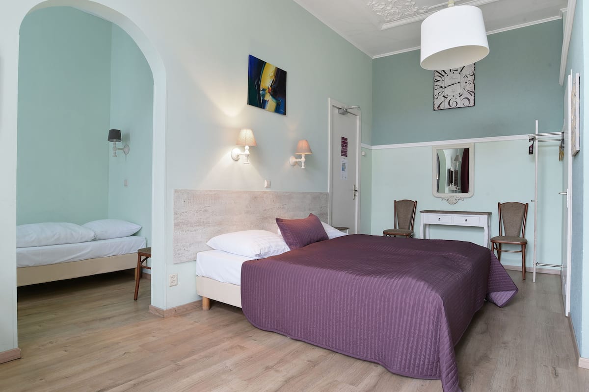 Una camera da letto con un letto, una scrivania, due sedie, uno specchio, una sveglia e un quadro appeso al muro.