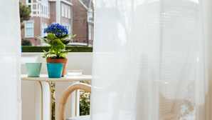 A balcony with a wicker chair, a small table, and a potted plant with blue flowers. - Hotel Corel (The Hague)