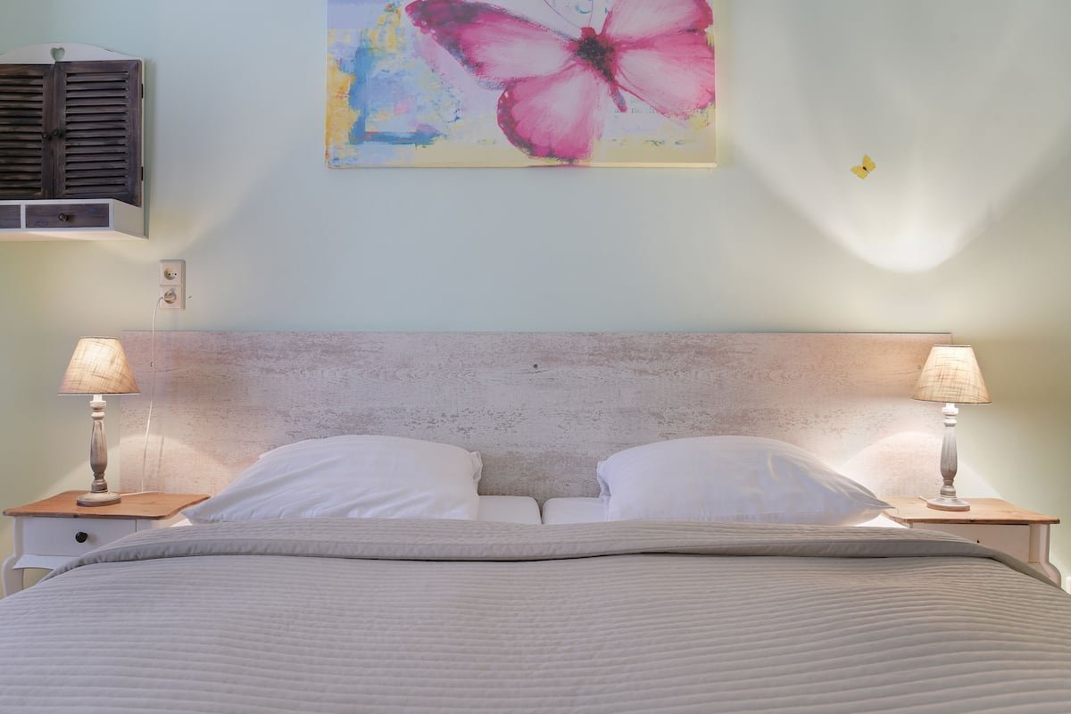 Un letto con una testiera, due comodini con lampade, una presa a muro e un quadro raffigurante una farfalla.