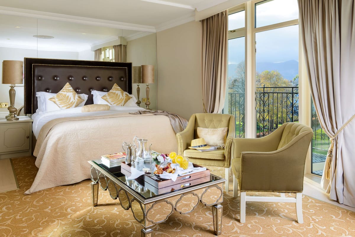 A hotel room with a large bed, a sitting area with a chair, a table with amenities, and a view of the outdoors.