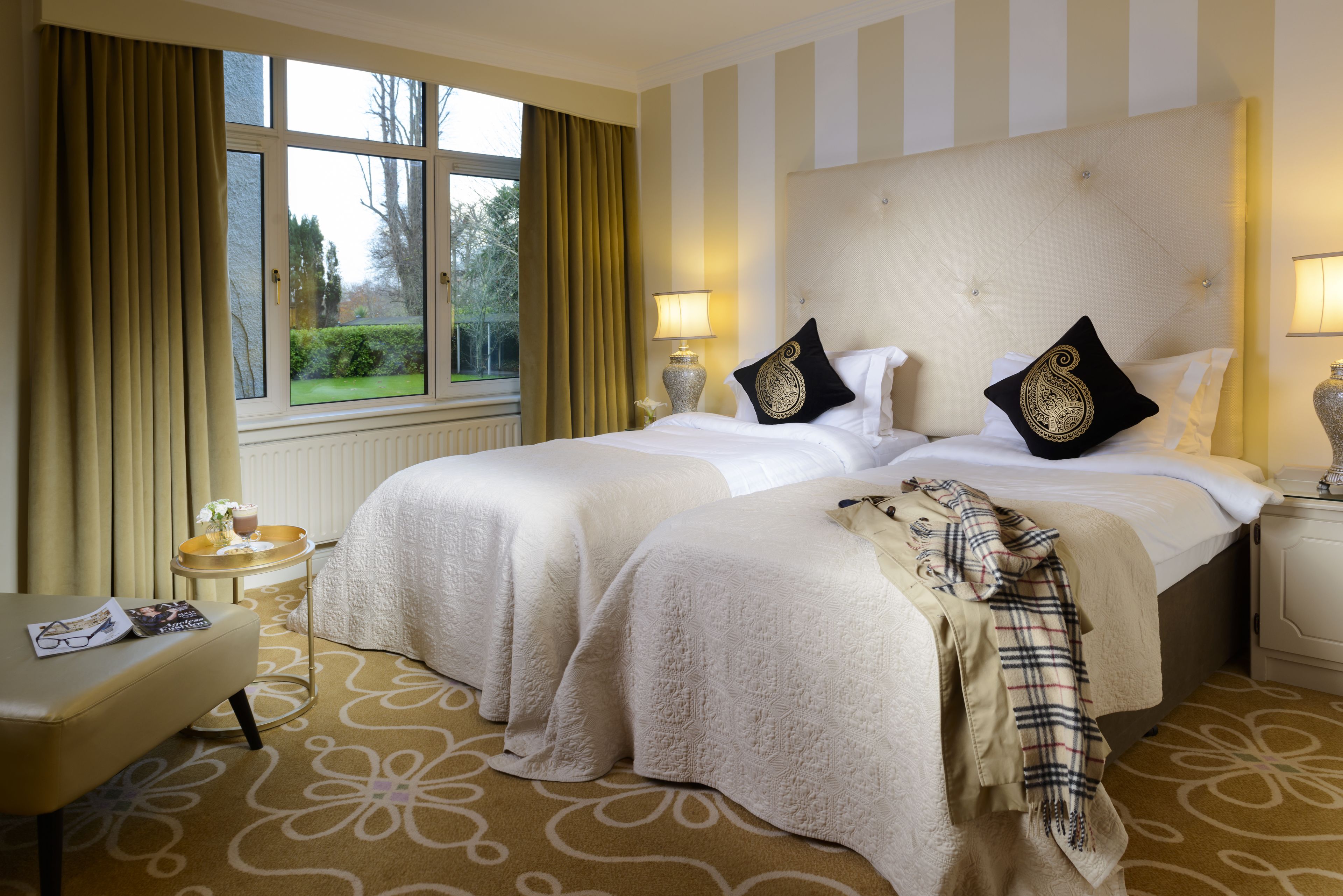 A hotel room with two beds, a small table with a tray, and a bench.