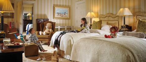 A hotel room with a large bed, a sitting area with a teddy bear, a dining table with breakfast items, and a painting on the wall.