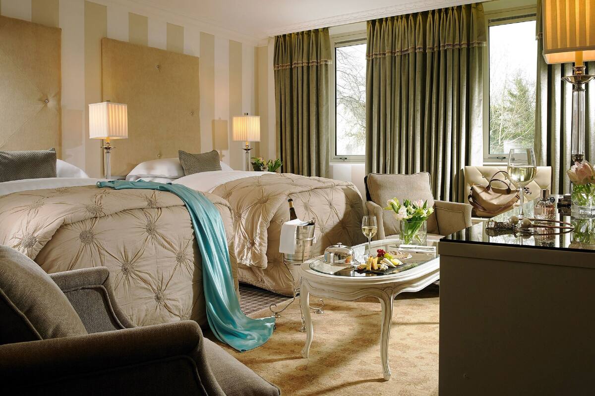 A hotel room with two beds, a sitting area with a table, and a view of the outdoors.