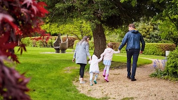 Una familia pasea por un parque con un árbol y esculturas al fondo.