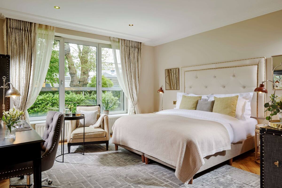 A spacious bedroom with a large bed, a desk, a chair, and a window with curtains.