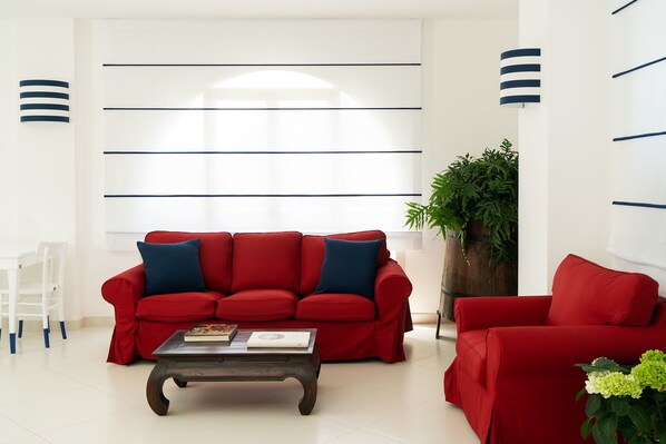 A modern living room with a red sofa, a wooden coffee table, and a white wall with horizontal lines. - Hotel Miramare (Sorrento)